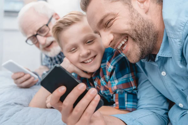 Lycklig familj med smartphone på säng — Stockfoto