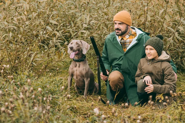 Otec a syn v podřepu v křoví na lovu — Stock fotografie