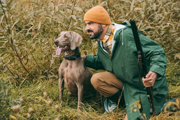 Homem agachando em arbustos com cão e arma — Fotografia de Stock