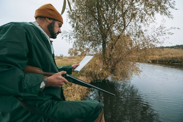 Jäger steht mit Gewehr und schaut auf Landkarte — kostenloses Stockfoto