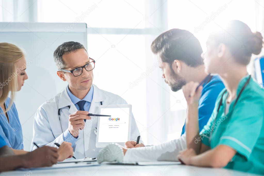 Young team of doctors and general practitioner having conversation and looking at tablet
