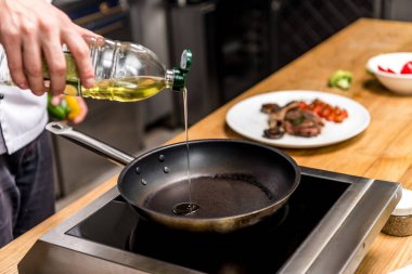 cropped image of chef pouring oil on frying pan clipart