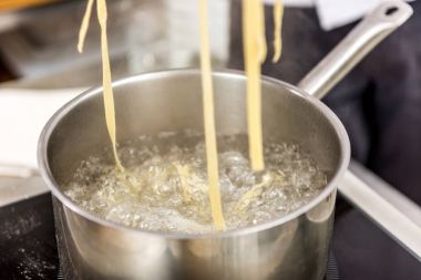 pasta in boiling water in pot on electric stove clipart