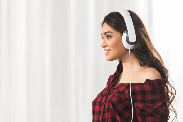 市松模様のシャツのヘッドフォンで音楽を聴くと 離れて見て微笑んでいる女の子の側面図 — ストック写真