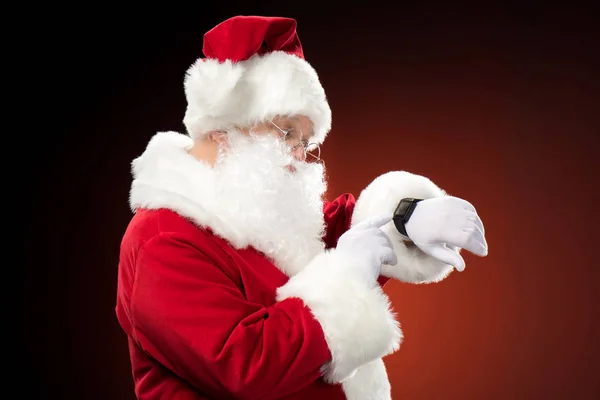 Papai Noel apontando no relógio inteligente — Fotografia de Stock