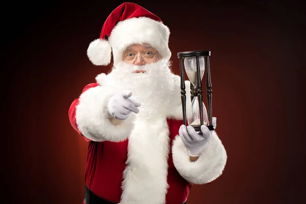 Santa Claus con reloj de arena apuntando a la cámara - foto de stock