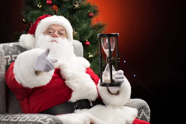 Santa Claus con reloj de arena apuntando a la cámara - foto de stock