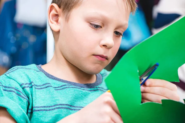 Школьник нарезает зеленую бумагу — стоковое фото