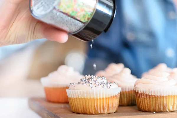 Donna mettendo coriandoli su cupcakes — Foto stock