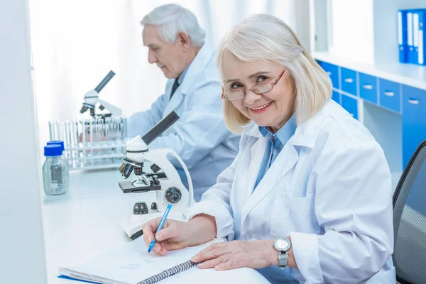 Químicos senior escribiendo en bloc de notas - foto de stock