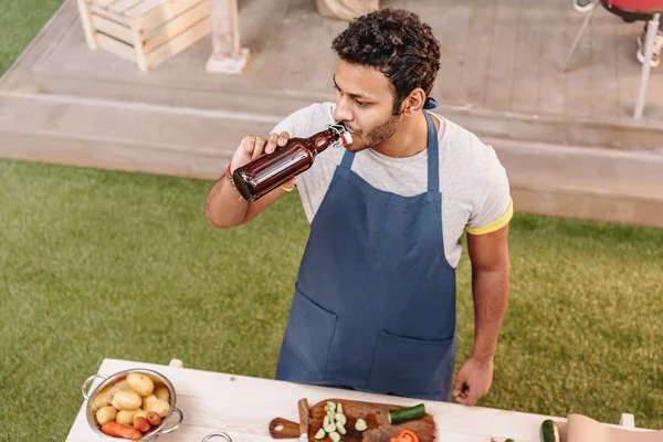 Man making burgers and drinking beer from bottle outdoors — Stock Photo