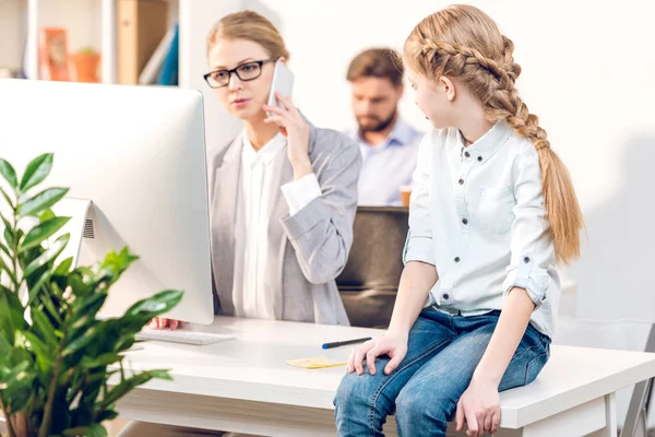 Daughter sitting on table in office — Stock Photo