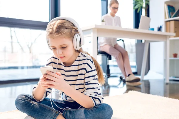 Hija usando smartphone y auriculares - foto de stock