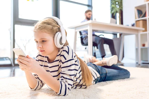 Tochter nutzt Smartphone und Kopfhörer — Stockfoto