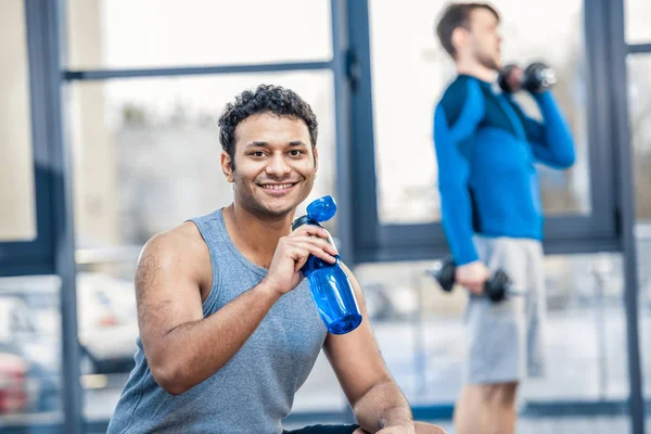 Hombre con botella de agua descansando en el gimnasio - foto de stock