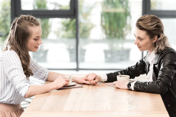 Girlfriends holding hands while drinking coffee — Stock Photo