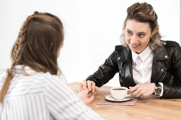 Girlfriends sitting at cafe and holding hands — Stock Photo