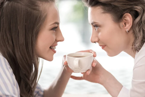 Young smiling girlfriends drinking coffee — Stock Photo