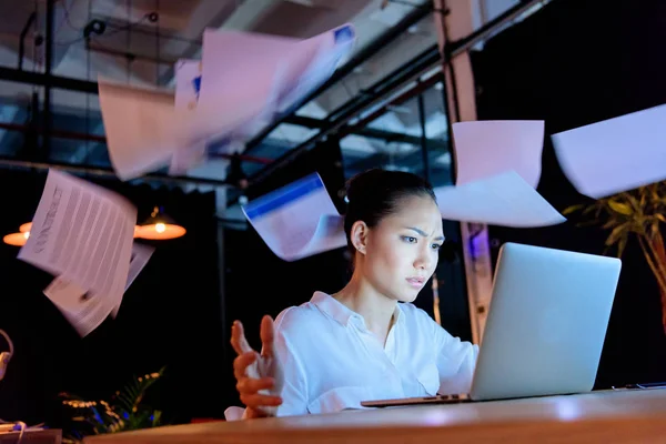 Businesswoman working on laptop and throwing documents — Stock Photo