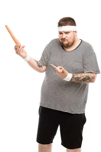 Fat man pointing with finger at carrot — Stock Photo