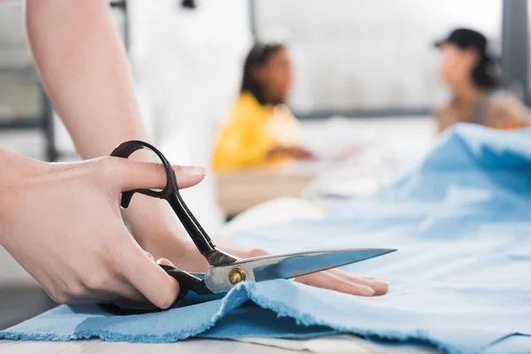 Young dressmaker cutting fabric with scissors — Stock Photo