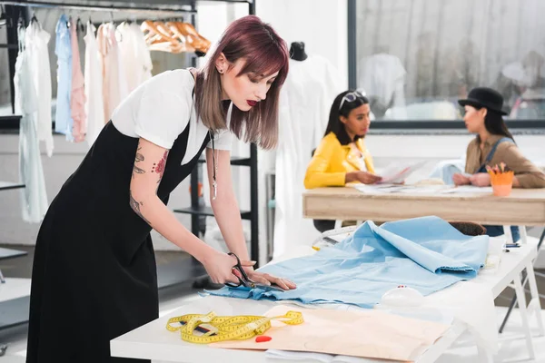 Dressmaker cutting blue fabric with scissors — Stock Photo