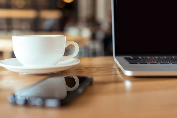 Taza de café y portátil en la mesa en la cafetería — Stock Photo