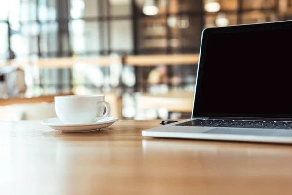 Tasse de café et ordinateur portable sur la table dans le café — Photo de stock