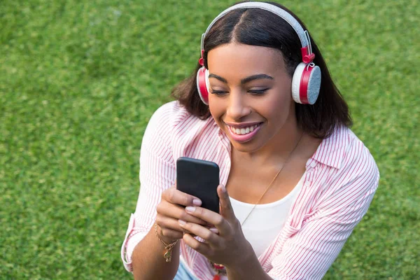 Chica en auriculares usando teléfono inteligente - foto de stock