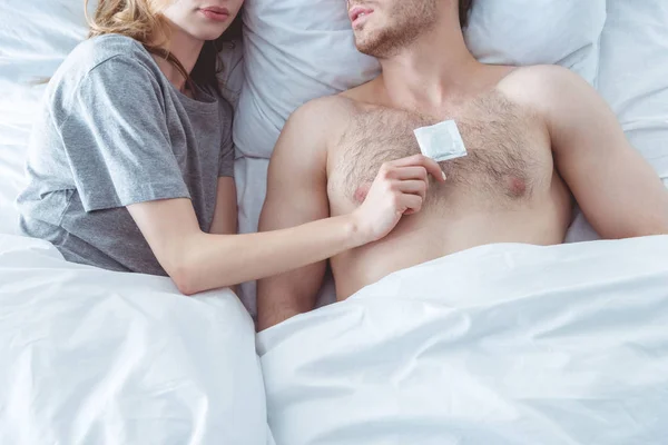 Pareja con condón en la cama - foto de stock