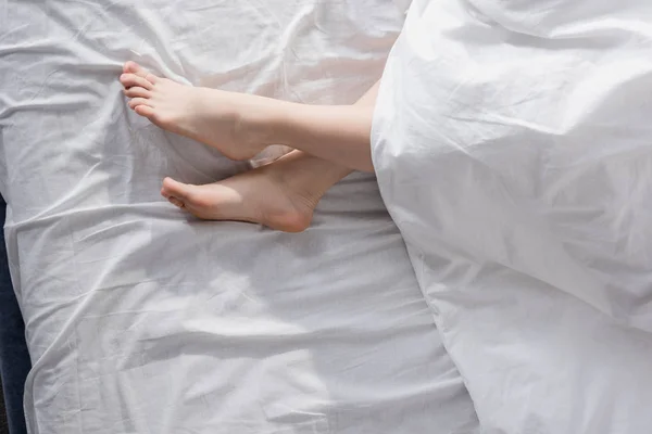 Pieds féminins s'étirant hors de la couverture — Photo de stock