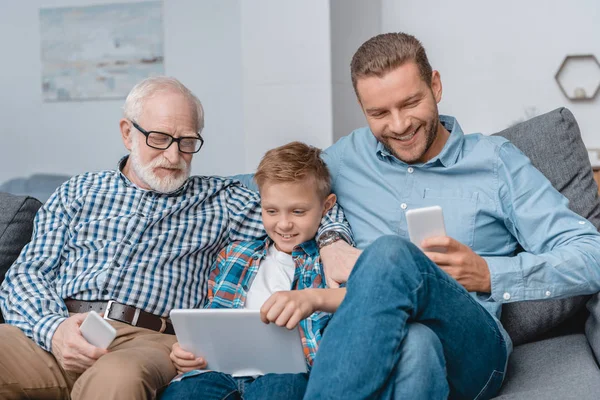 Familia sentada en el sofá con dispositivos - foto de stock