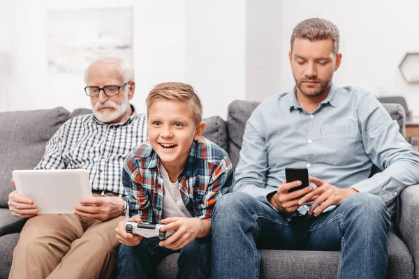 Familia sentada en el sofá con dispositivos - foto de stock