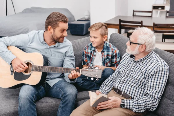 Padre tocando la guitarra con la familia en casa - foto de stock