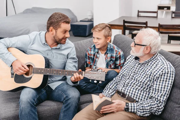 Padre tocando la guitarra con la familia en casa - foto de stock