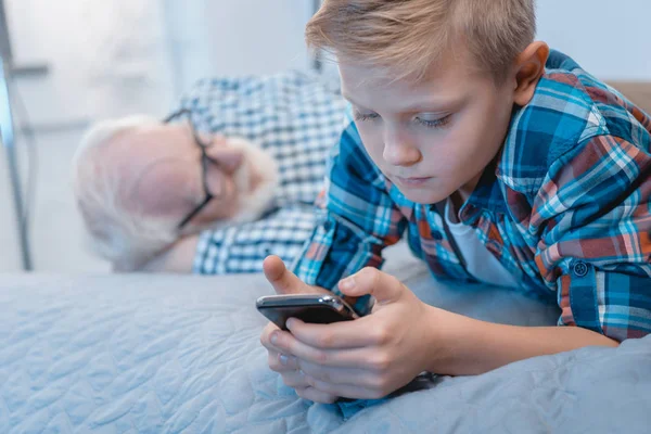 Little boy using smartphone on bed — Stock Photo