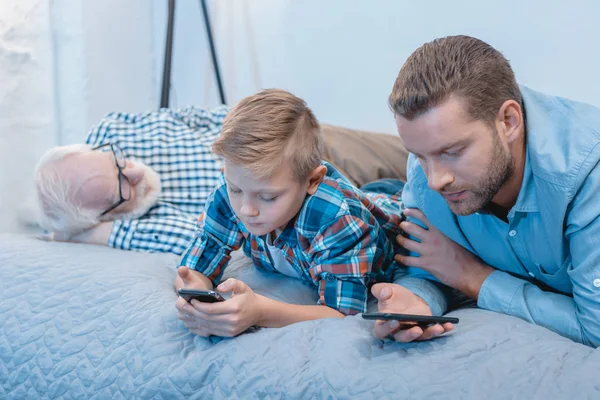 Garçon et père avec samrtphones sur le lit — Photo de stock