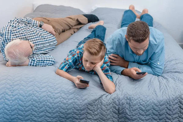 Menino e pai com samrtphones na cama — Fotografia de Stock