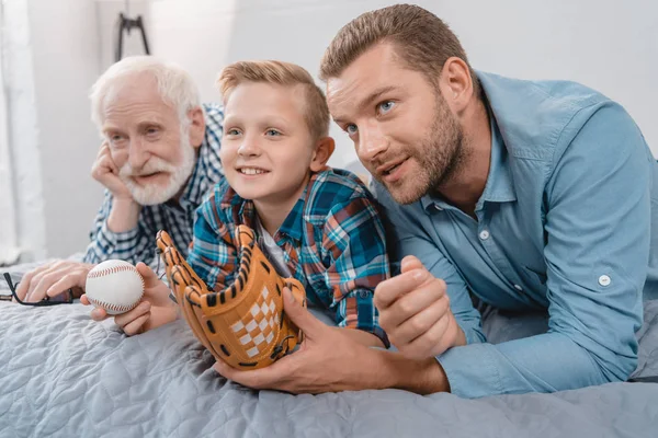 Family watching baseball game on bed — Stock Photo