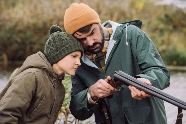 Padre mostrando hijo cómo cargar arma - foto de stock