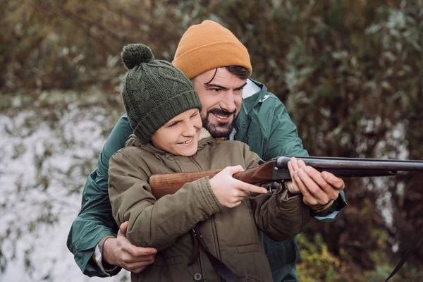 Padre ayudando a su hijo apuntando con arma - foto de stock