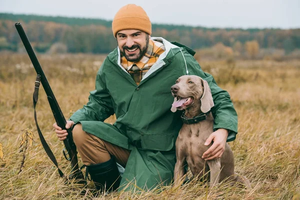 Man squatting with dog and gun — Stock Photo