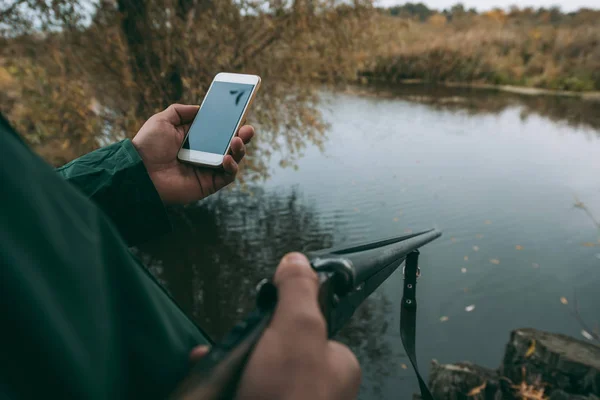 Homem de pé com arma e olhando para o smartphone — Fotografia de Stock