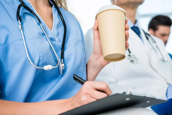 Nurse with coffee writing in clipboard — Stock Photo