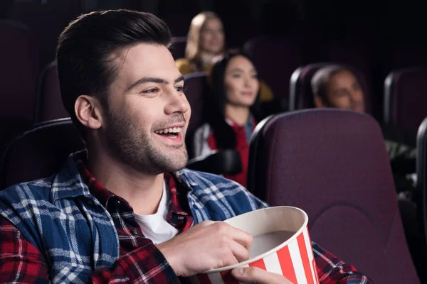 Smiling handsome man with popcorn watching movie in cinema — Stock Photo