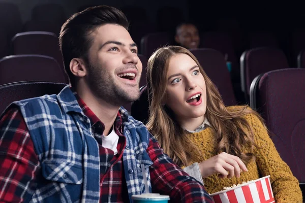 Young smiling couple with popcorn watching movie in cinema — Stock Photo