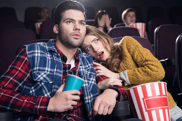 Frightened couple with popcorn watching horror movie in cinema — Stock Photo