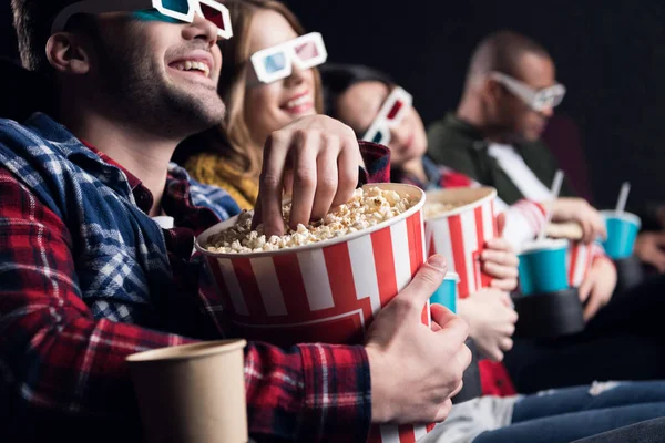 Jóvenes amigos sonrientes en gafas 3d comiendo palomitas de maíz y viendo películas en el cine - foto de stock