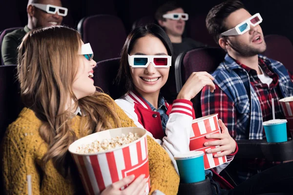 Jeunes amis souriants dans des lunettes 3D avec du pop-corn regarder un film au cinéma — Photo de stock