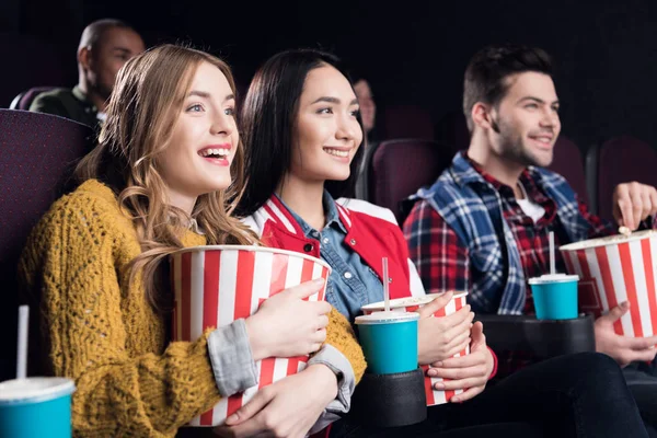 Young smiling friends with popcorn watching film in movie theater — Stock Photo